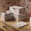A set of decorative storage boxes with a blue and white toile de Jouy pattern, arranged on a beige wooden vanity table against a matching floral wallpaper background. Featuring an A5 notebook for sale.