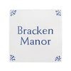 A square white decorative tile or plaque with the words 'Bracken Manor' printed in blue serif text, with small blue floral corner motifs, shown on a plain white background.