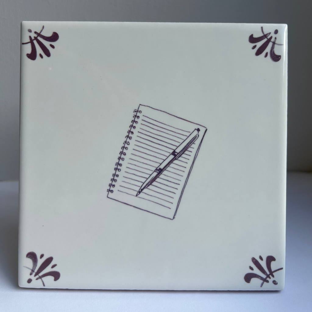 manganese delft tile with corners and pictorial design of a notebook and pen