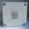 A square ceramic tile with a glossy white glaze, featuring a hand-painted illustration of french fries in a striped bucket in the center and matching manganeses corner flourishes.