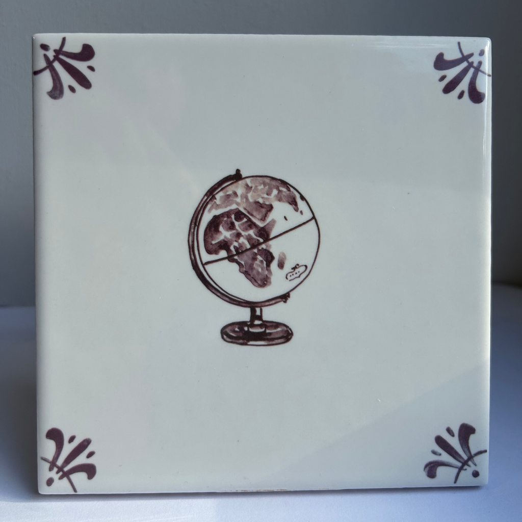 A square ceramic tile with a glossy off-white background, featuring a central manganese  illustration of a globe and four matching decorative corner flourishes in manganese 